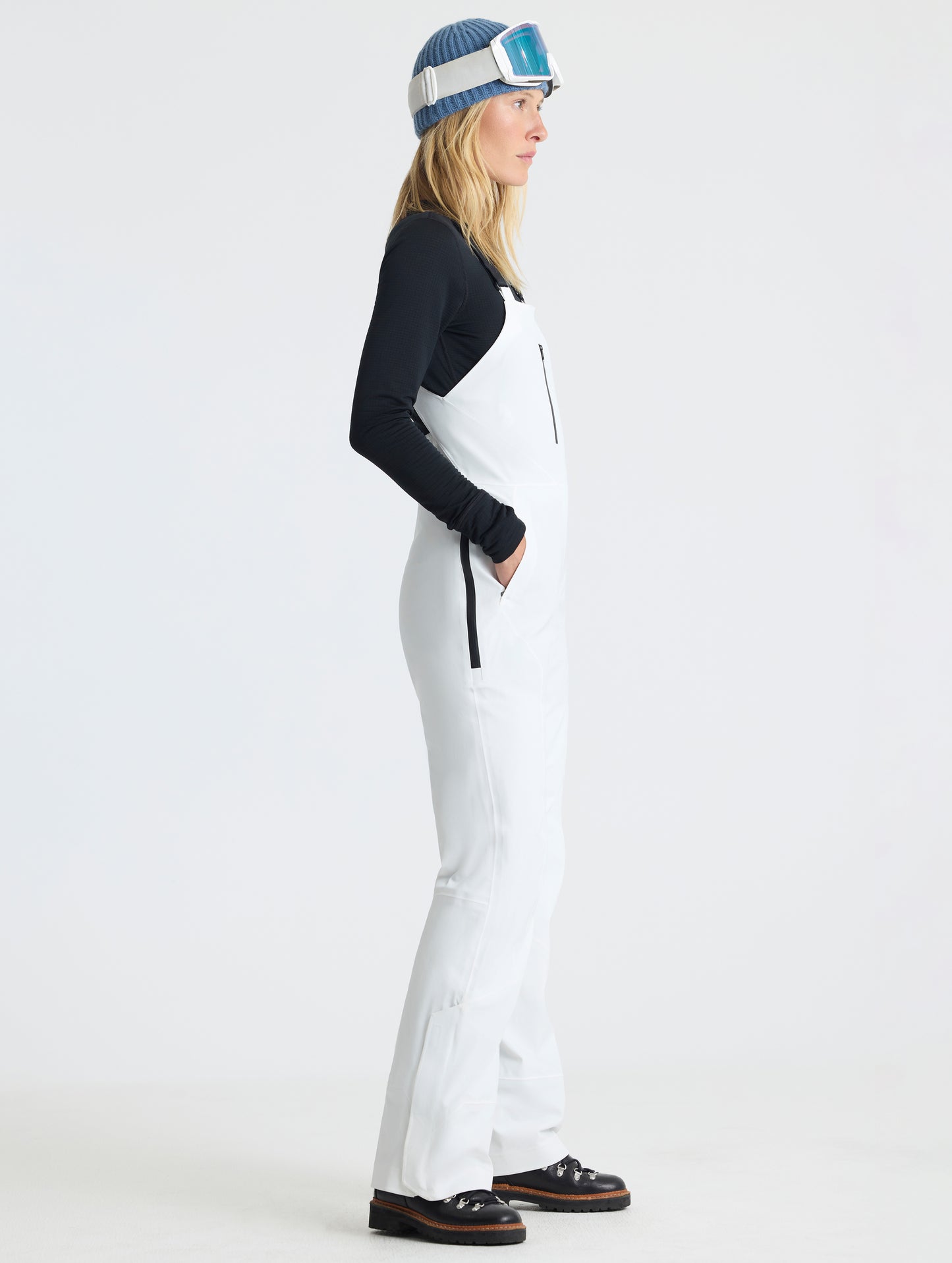Side profile full-body view of woman wearing the Sophia Insulated Snow Bib in Winter White from AETHER Apparel.