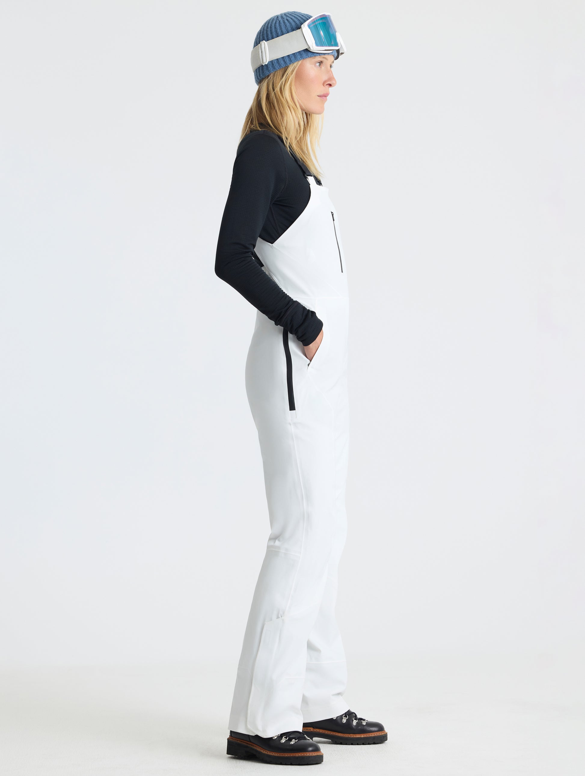 Side profile full-body view of woman wearing the Sophia Insulated Snow Bib in Winter White from AETHER Apparel.