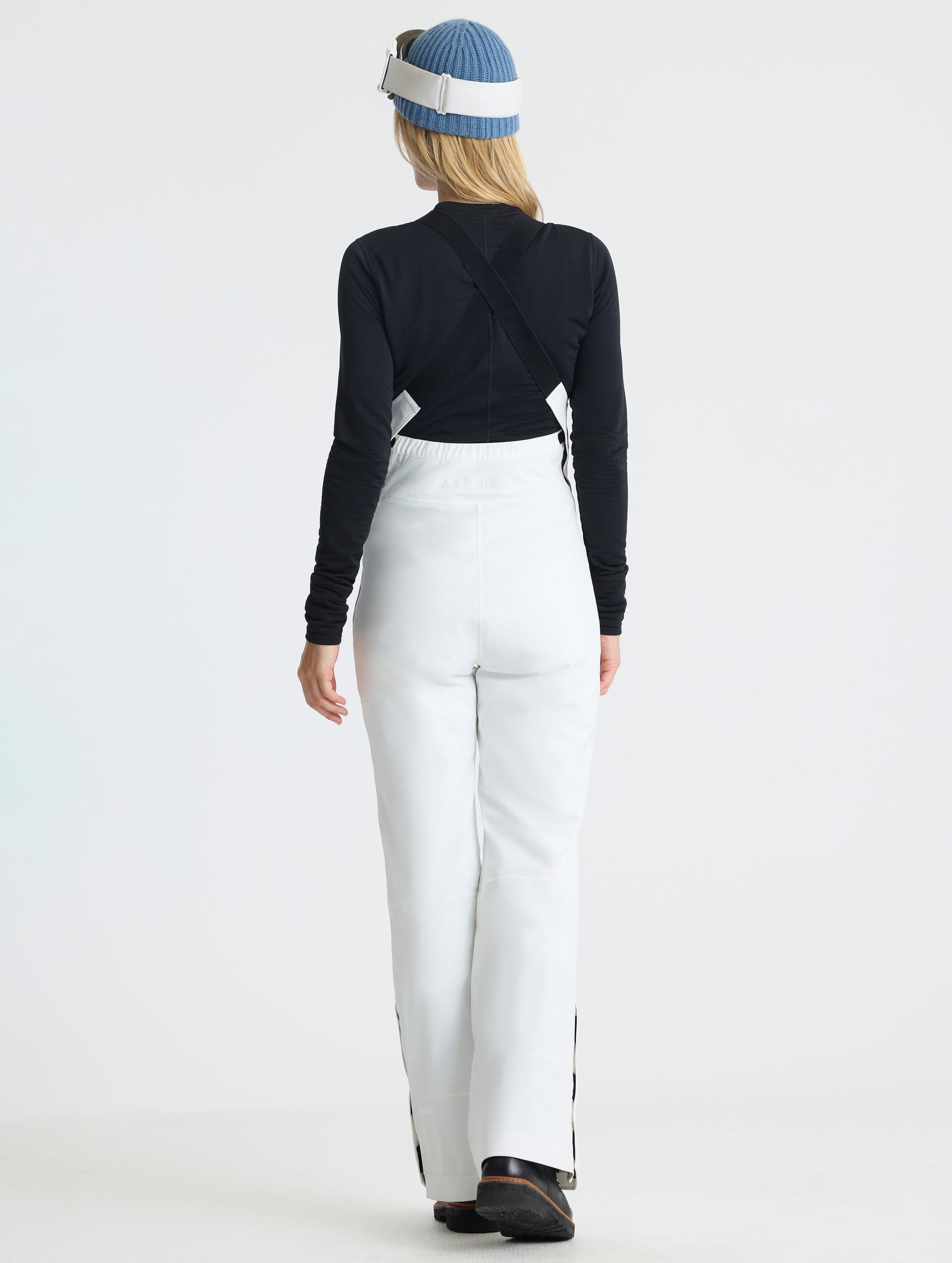 Rear full-body view of woman wearing the Sophia Insulated Snow Bib in Winter White from AETHER Apparel.
