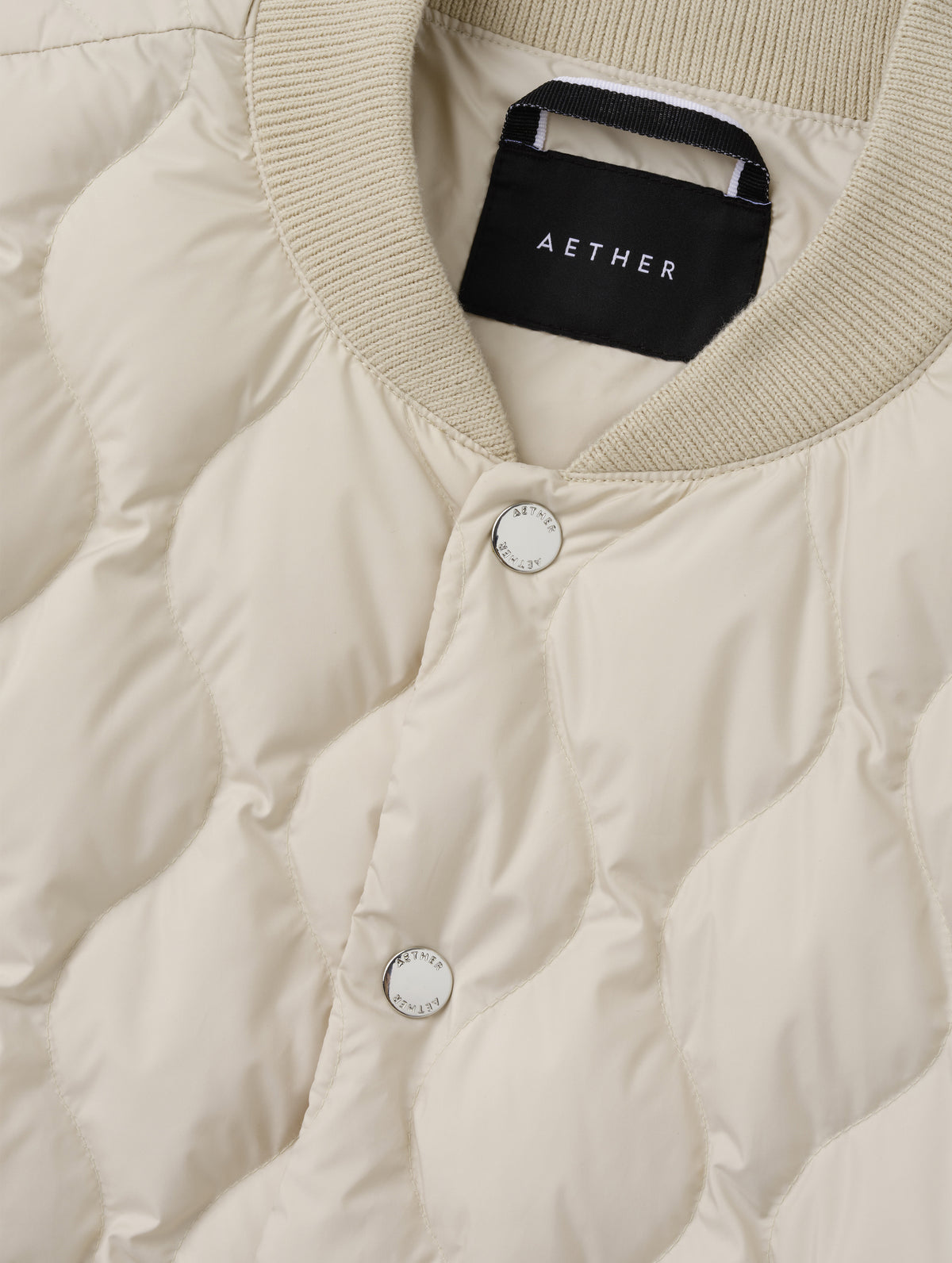 Closeup detailed view of the center-front snap closure, locker loop, and rib-knit collar on the Stella Liner Jacket in Bone from AETHER Apparel.