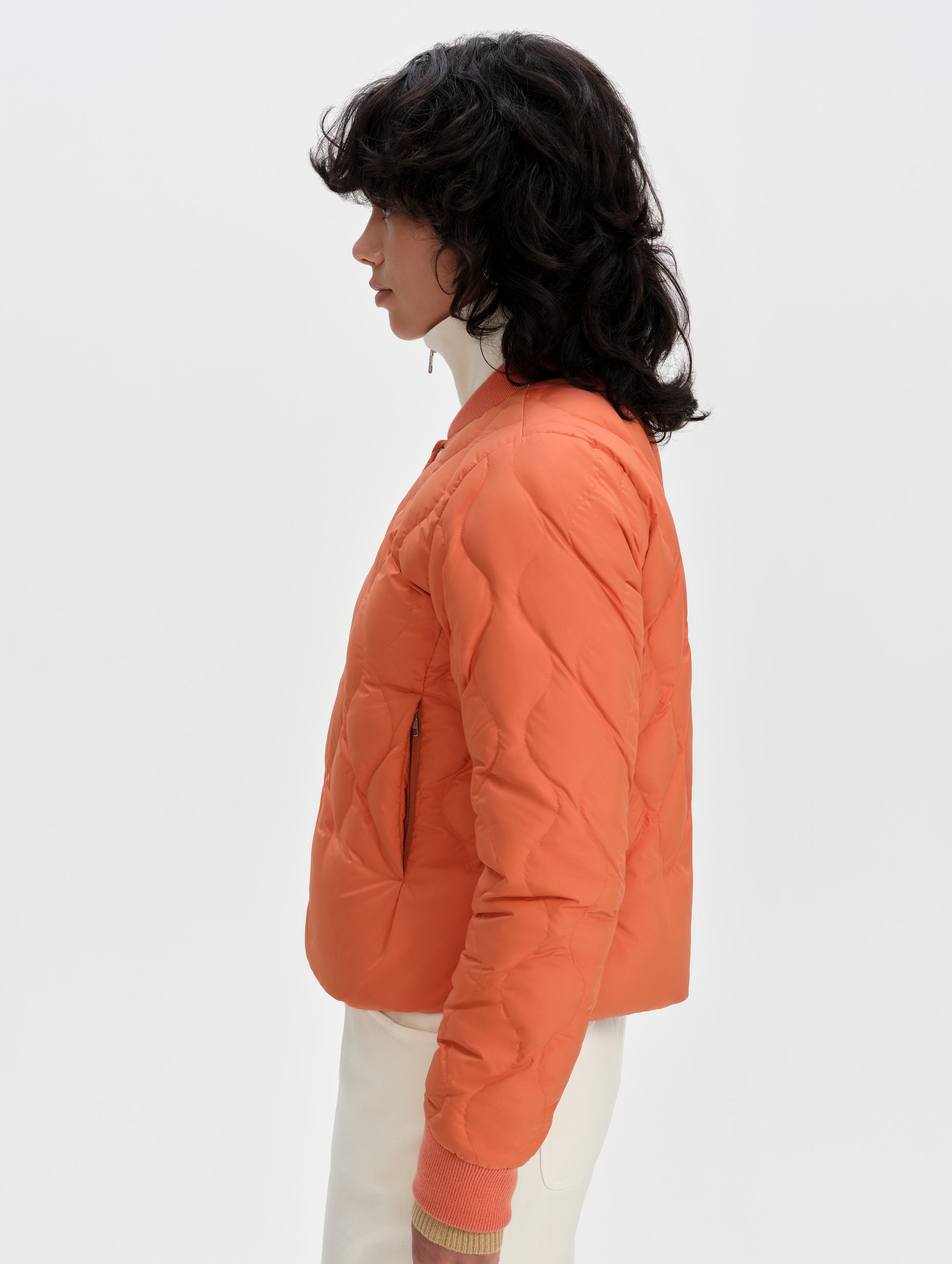 Side profile upper-body view of woman wearing the Stella Liner Jacket in Madeira Orange from AETHER Apparel.