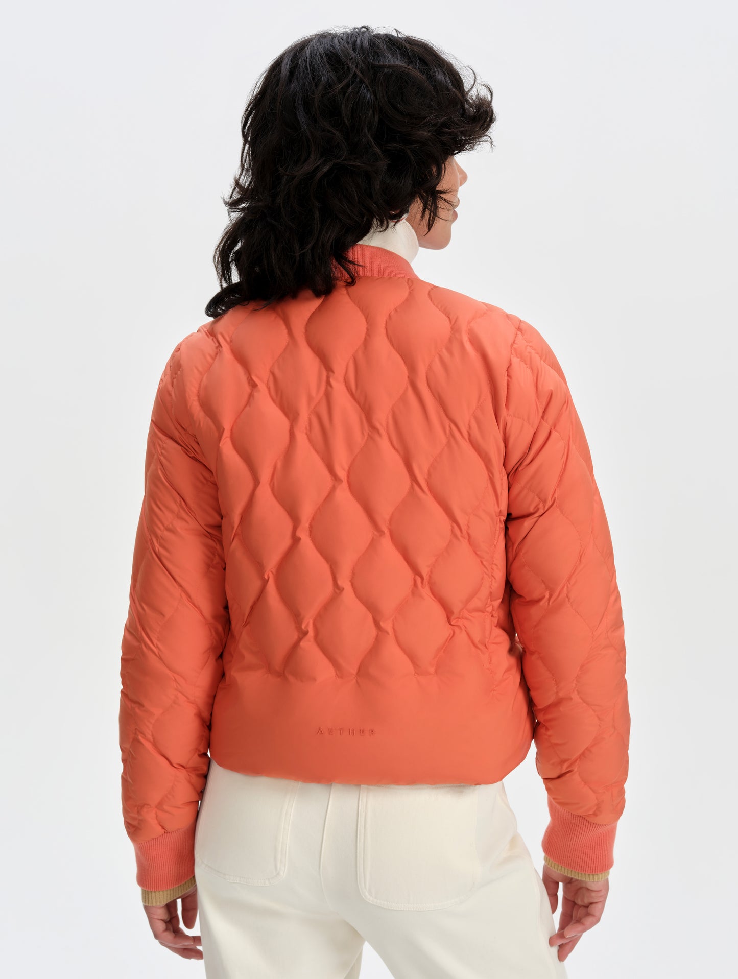 Rear upper-body view of woman wearing the Stella Liner Jacket in Madeira Orange from AETHER Apparel.