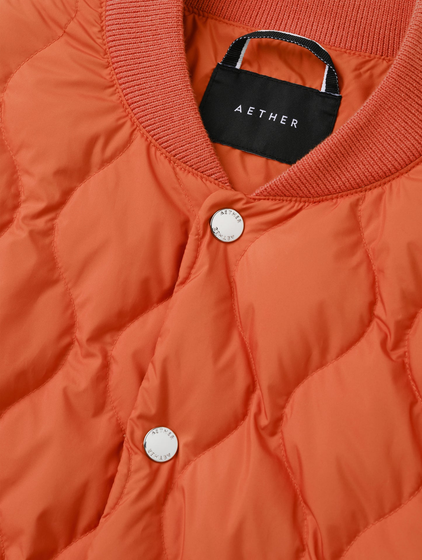 Closeup detailed view of the center-front snap closure, locker loop, and rib-knit collar on the Stella Liner Jacket in Madeira Orange from AETHER Apparel.