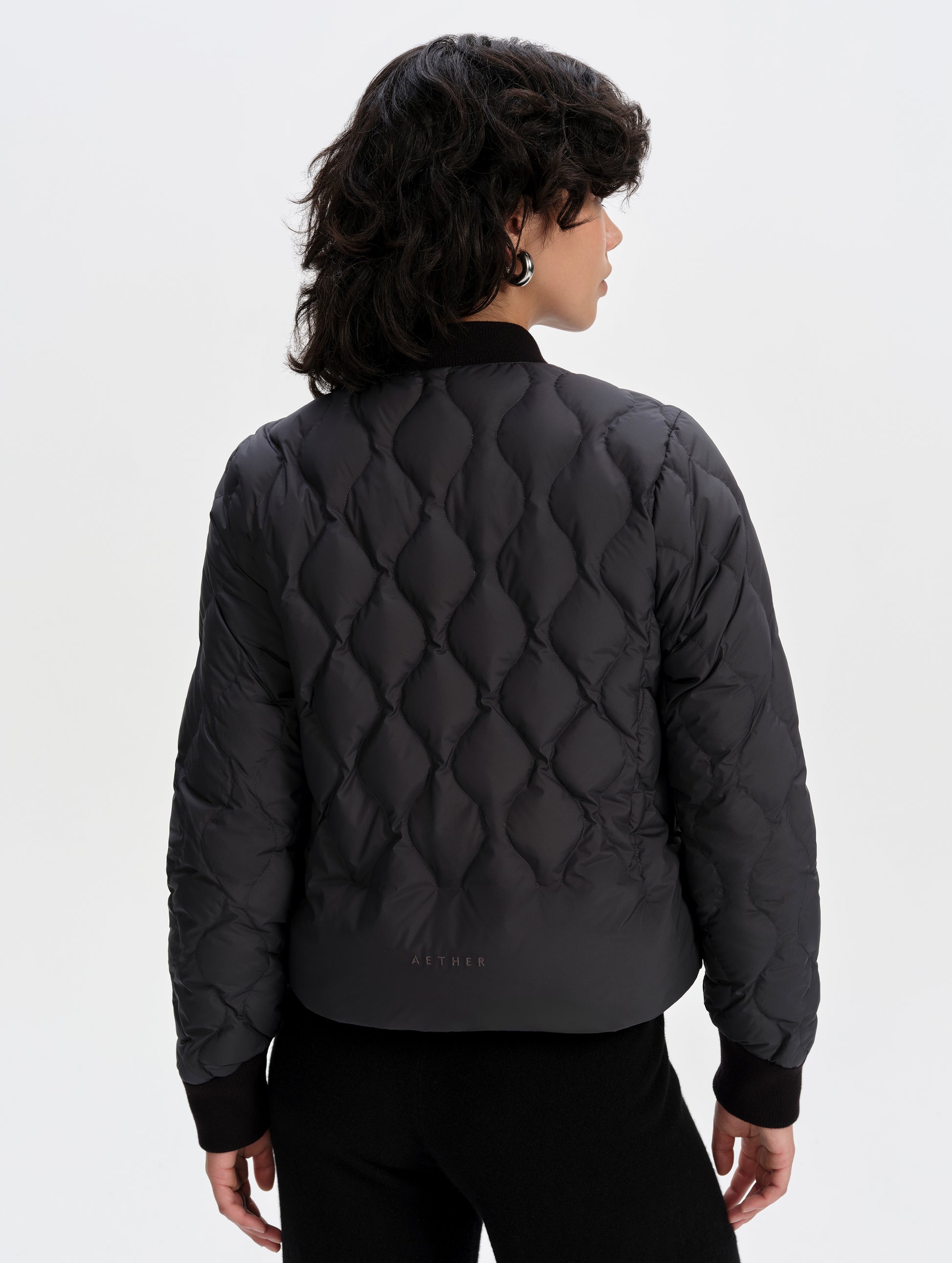 Rear upper-body view of woman wearing the Stella Liner Jacket in Onyx Black from AETHER Apparel.