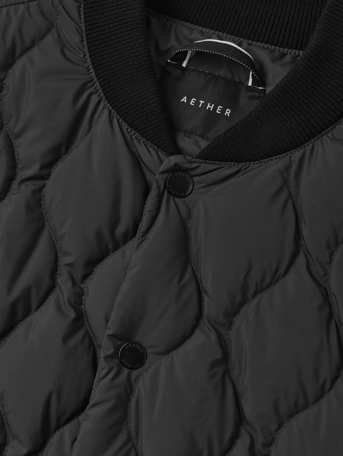 Closeup detailed view of the center-front snap closure, locker loop, and rib-knit collar on the Stella Liner Jacket in Onyx Black from AETHER Apparel.