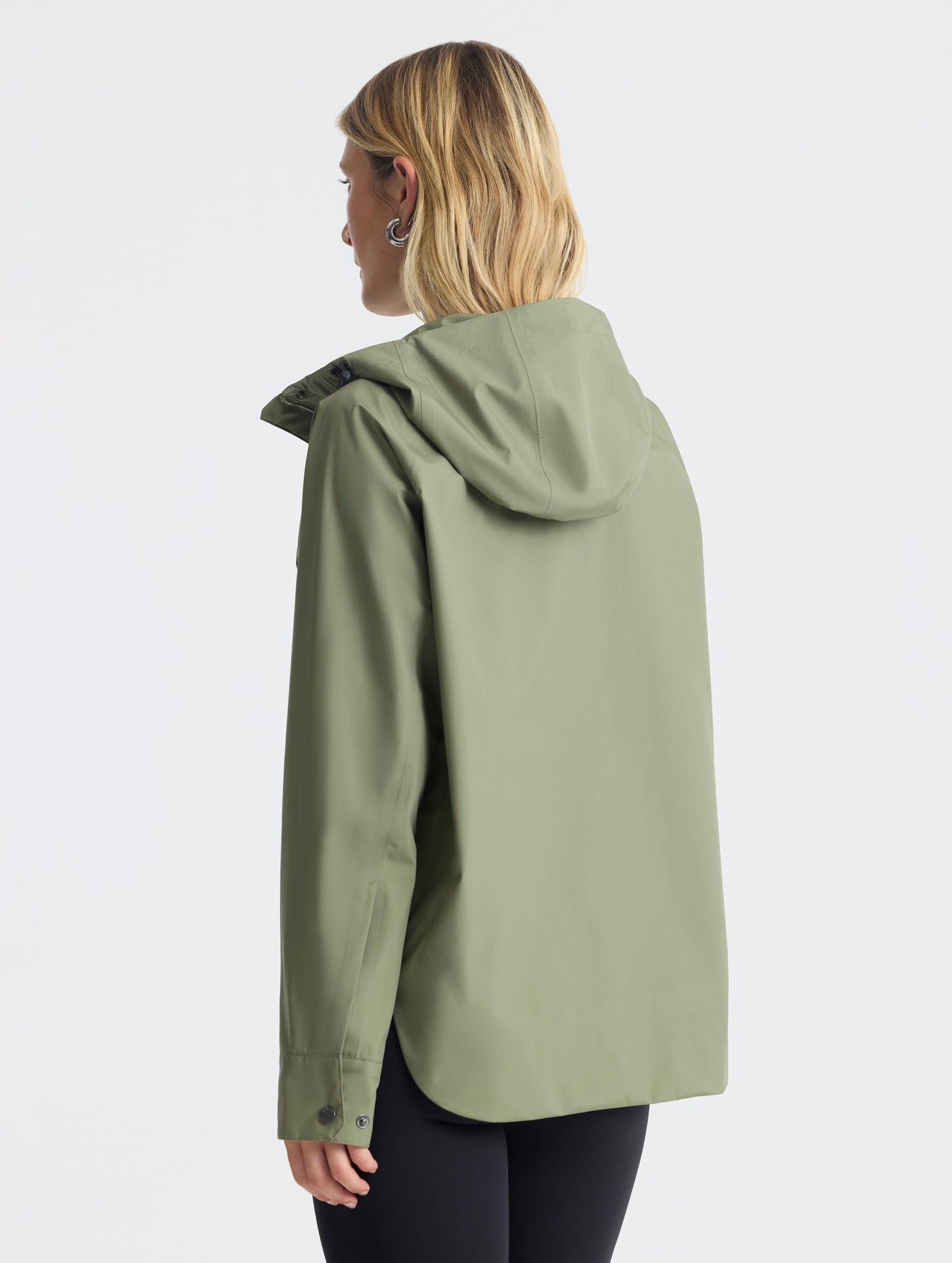 Rear angled view of woman wearing Storm All-Weather Jacket in Fern Green from AETHER Apparel.