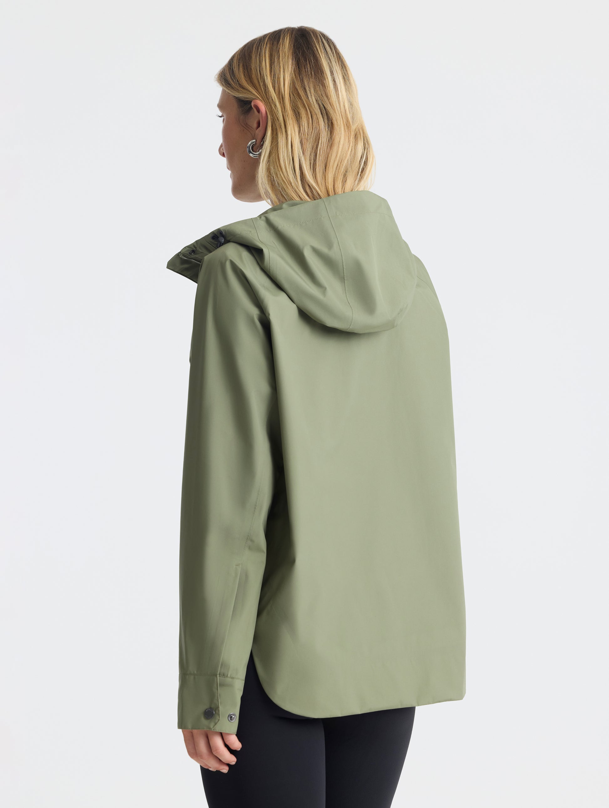 Rear angled view of woman wearing Storm All-Weather Jacket in Fern Green from AETHER Apparel.