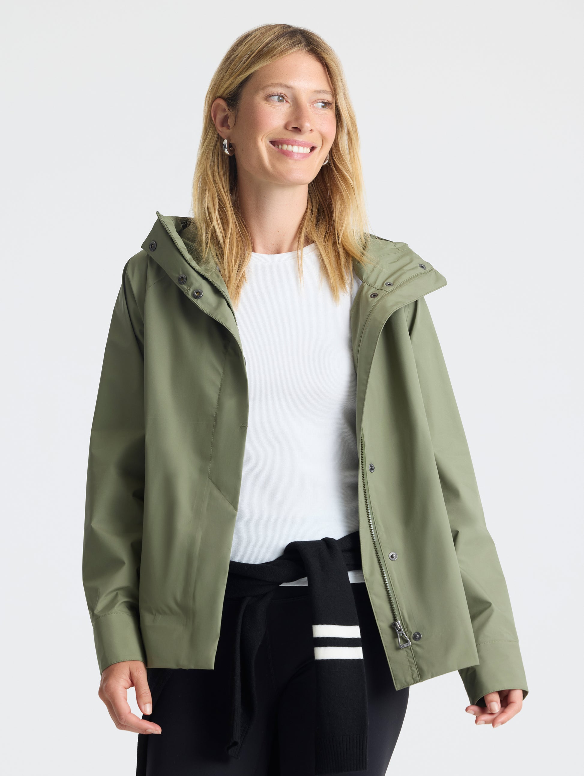 Front view of woman wearing unzipped Storm All-Weather Jacket in Fern Green from AETHER Apparel.