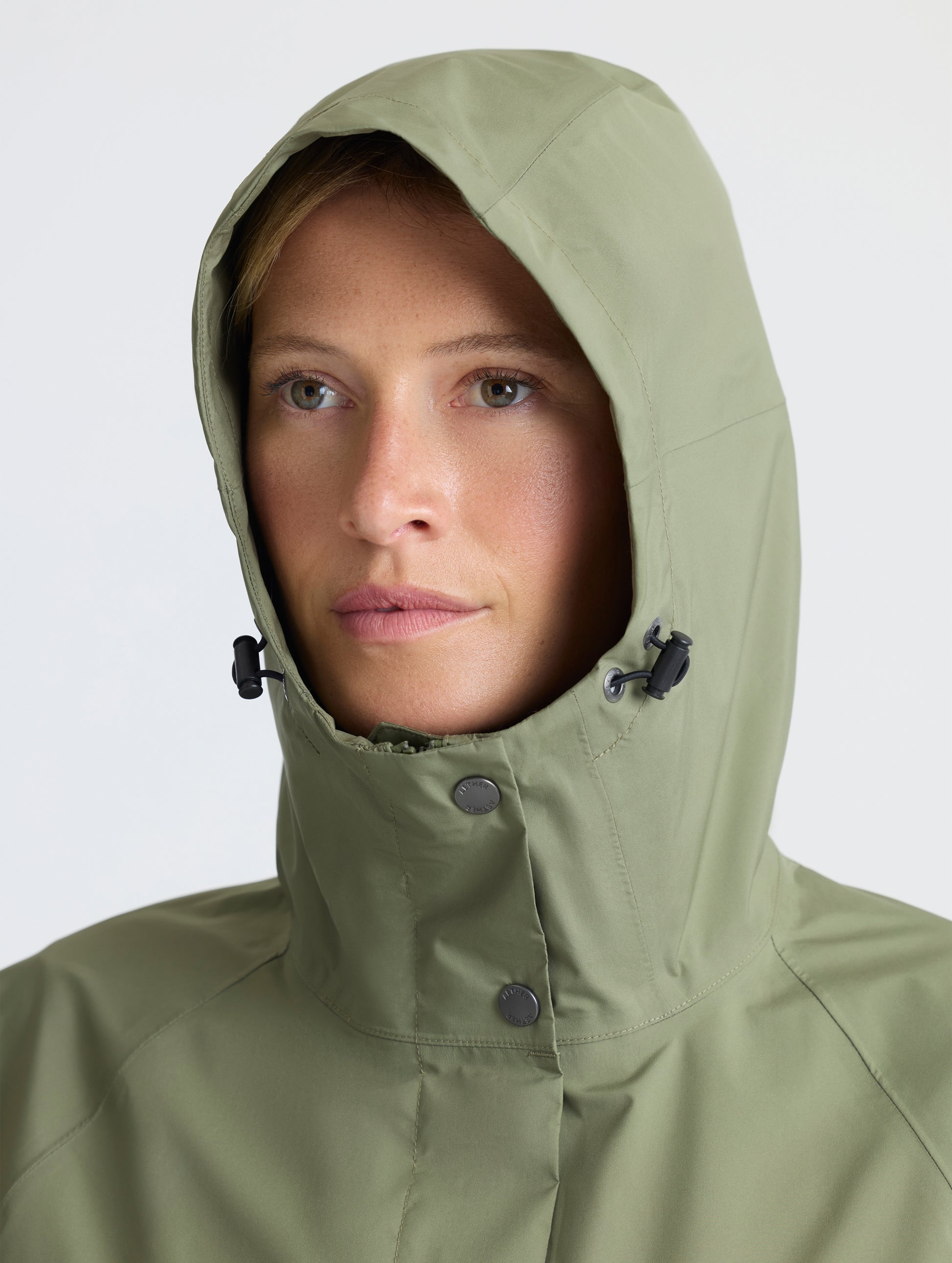 Closeup view of woman wearing hood of Storm All-Weather Jacket in Fern Green from AETHER Apparel.