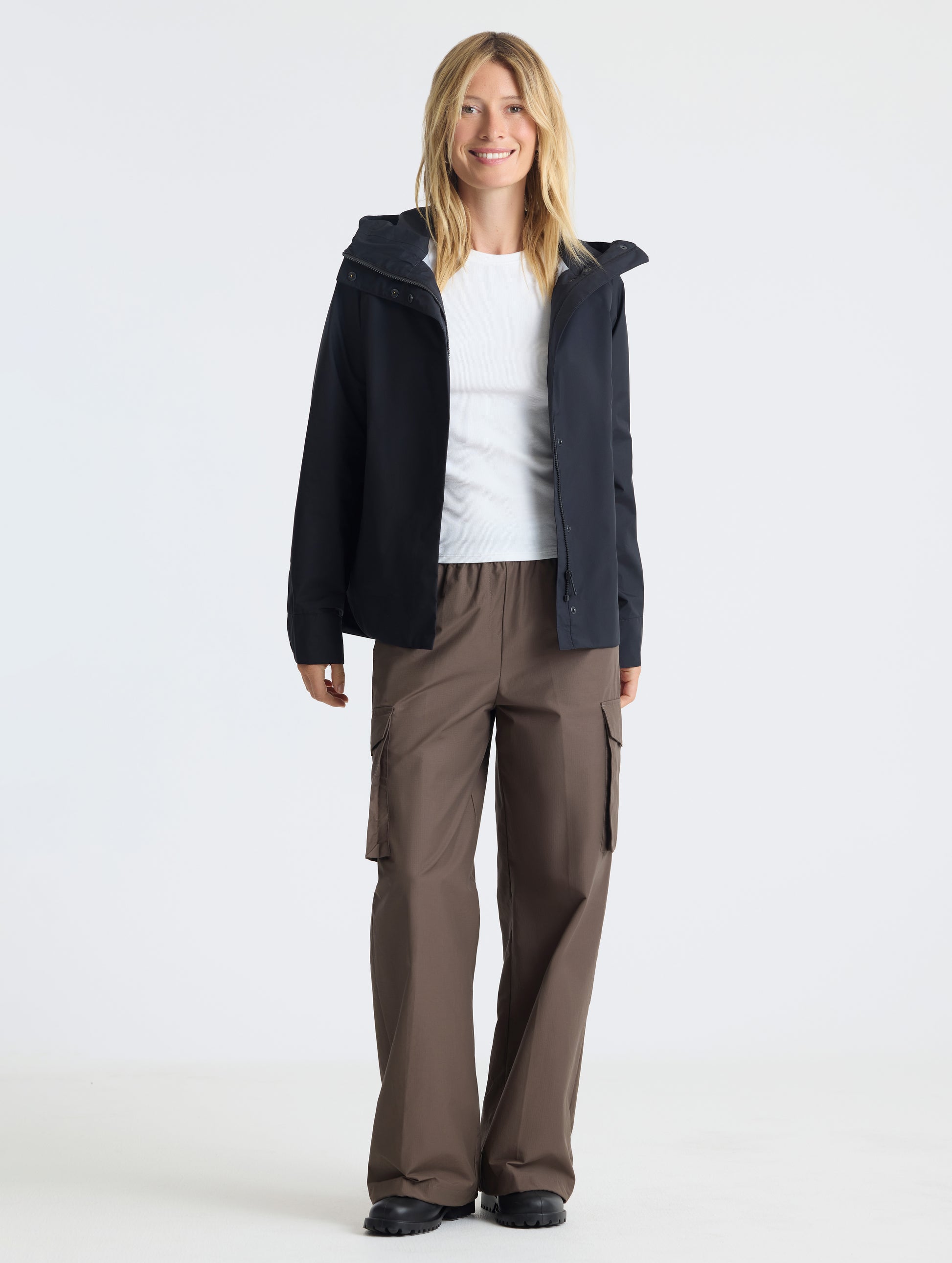 Front, full-body view of woman wearing Storm All-Weather Jacket in Onyx Black from AETHER Apparel.