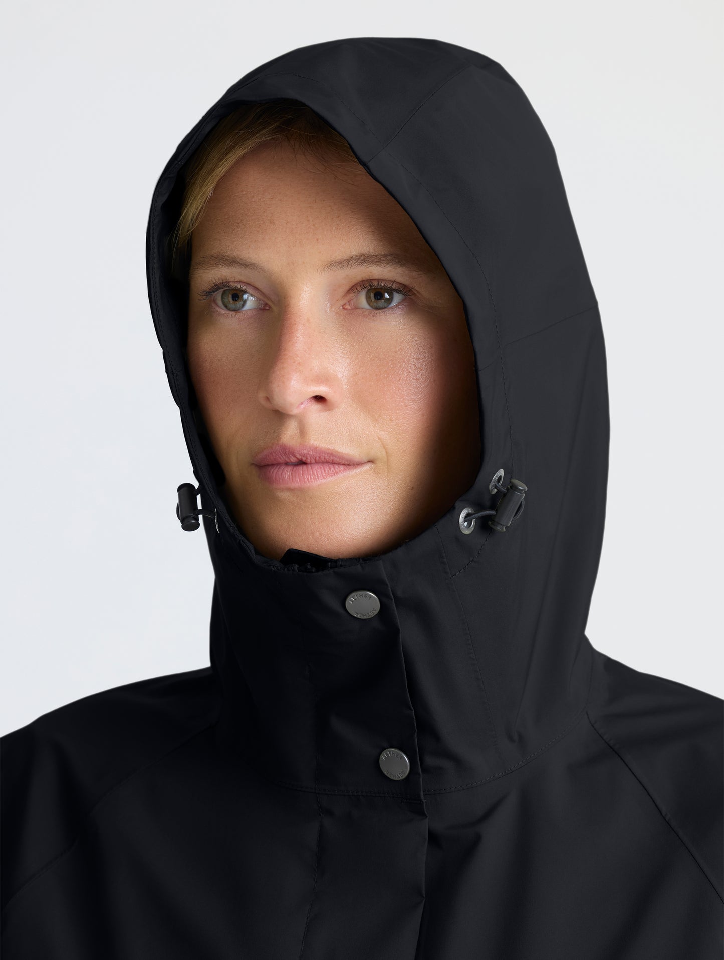 Closeup view of woman wearing hood of Storm All-Weather Jacket in Onyx Black from AETHER Apparel.