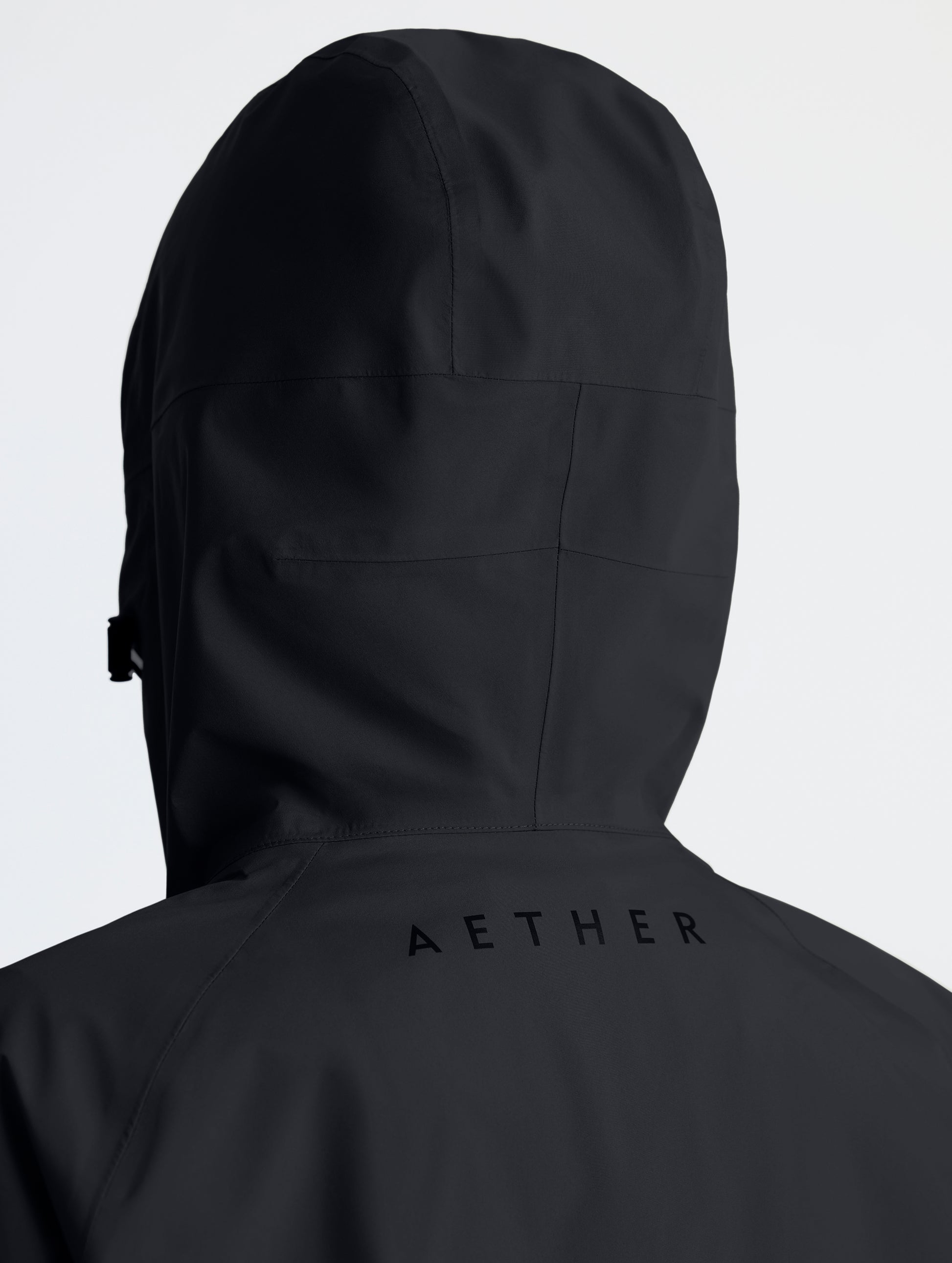 Rear view of woman wearing hood of Storm All-Weather Jacket in Onyx Black from AETHER Apparel.