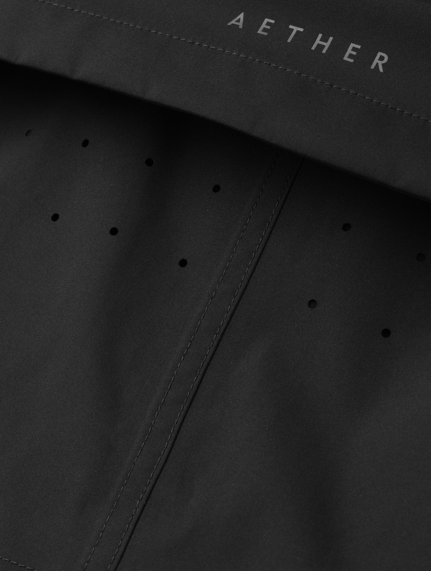 Closeup detailed view of the laser-cut ventilation holes and storm flap on the women's Wallace Rain Parka in Onyx Black from AETHER Apparel.