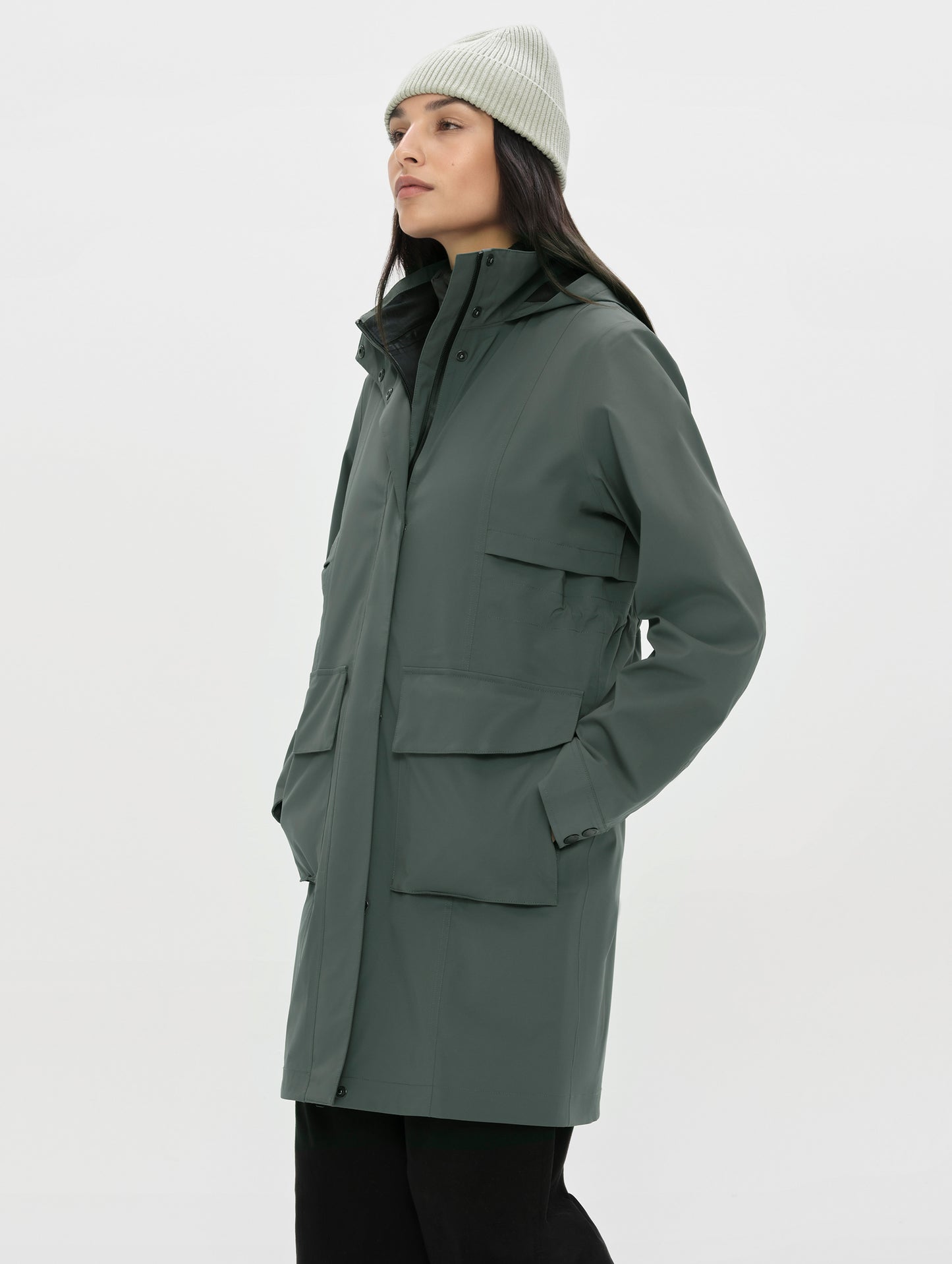 Front, angled upper-body view of woman wearing the zipped up Wallace Rain Parka in Saville Green from AETHER Apparel.