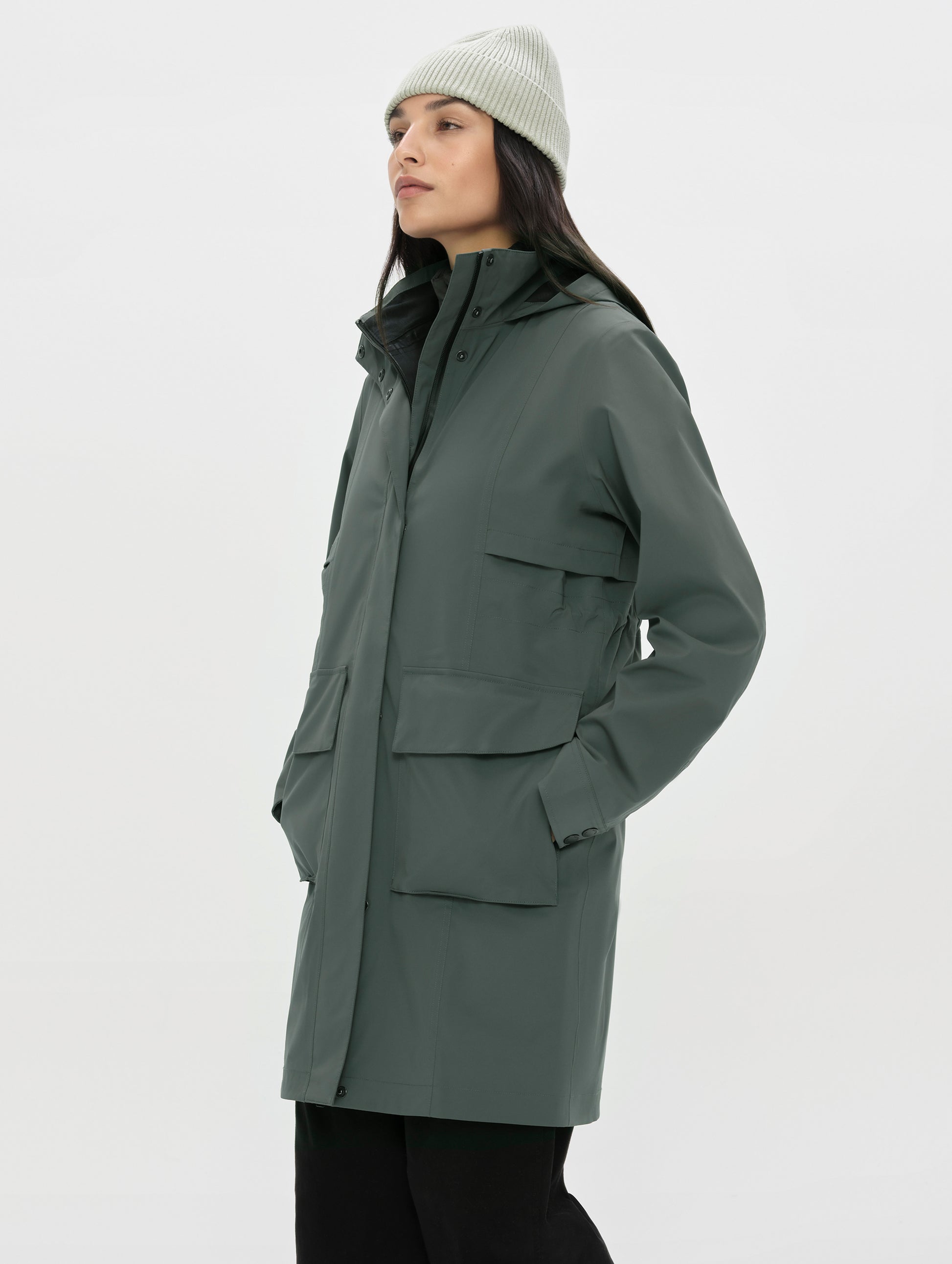 Front, angled upper-body view of woman wearing the zipped up Wallace Rain Parka in Saville Green from AETHER Apparel.