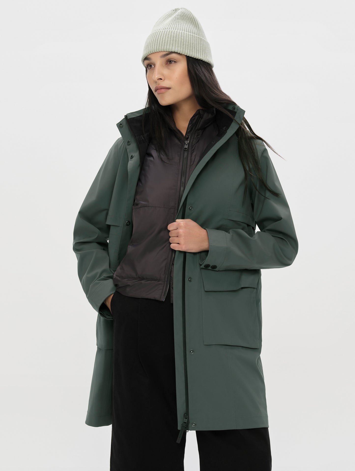 Front, angled upper-body view of woman wearing the unzipped Wallace Rain Parka in Saville Green from AETHER Apparel.