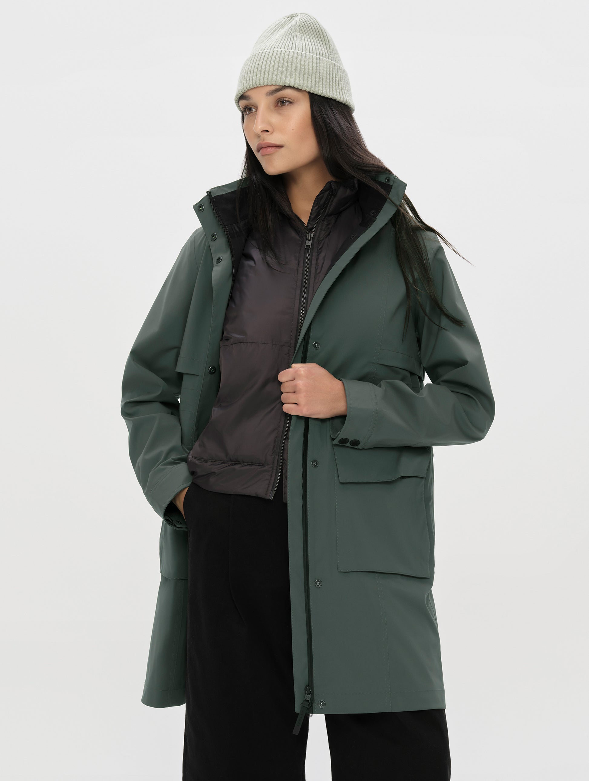Front, angled upper-body view of woman wearing the unzipped Wallace Rain Parka in Saville Green from AETHER Apparel.