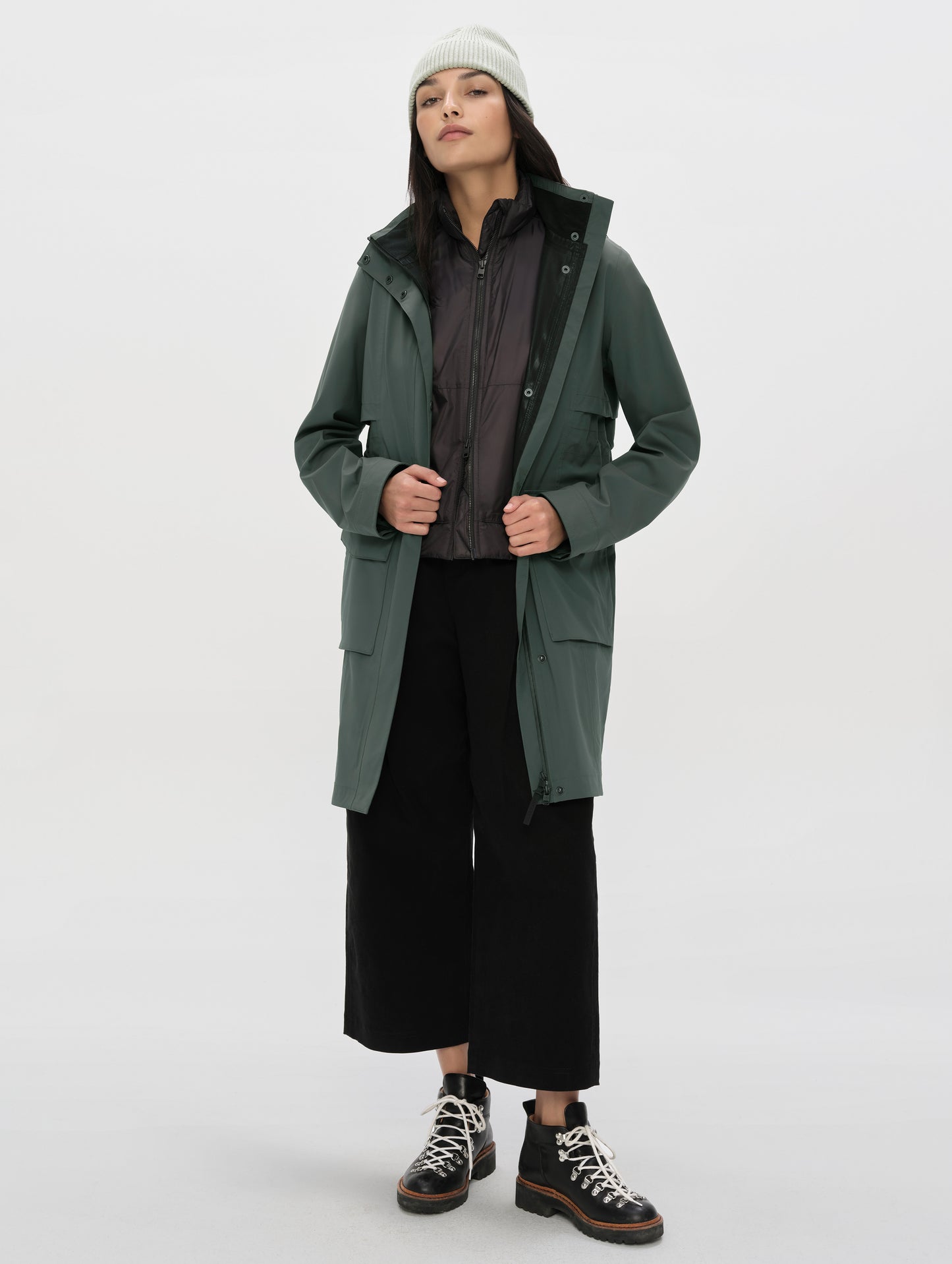 Front full-body view of woman wearing the unzipped Wallace Rain Parka in Saville Green from AETHER Apparel.