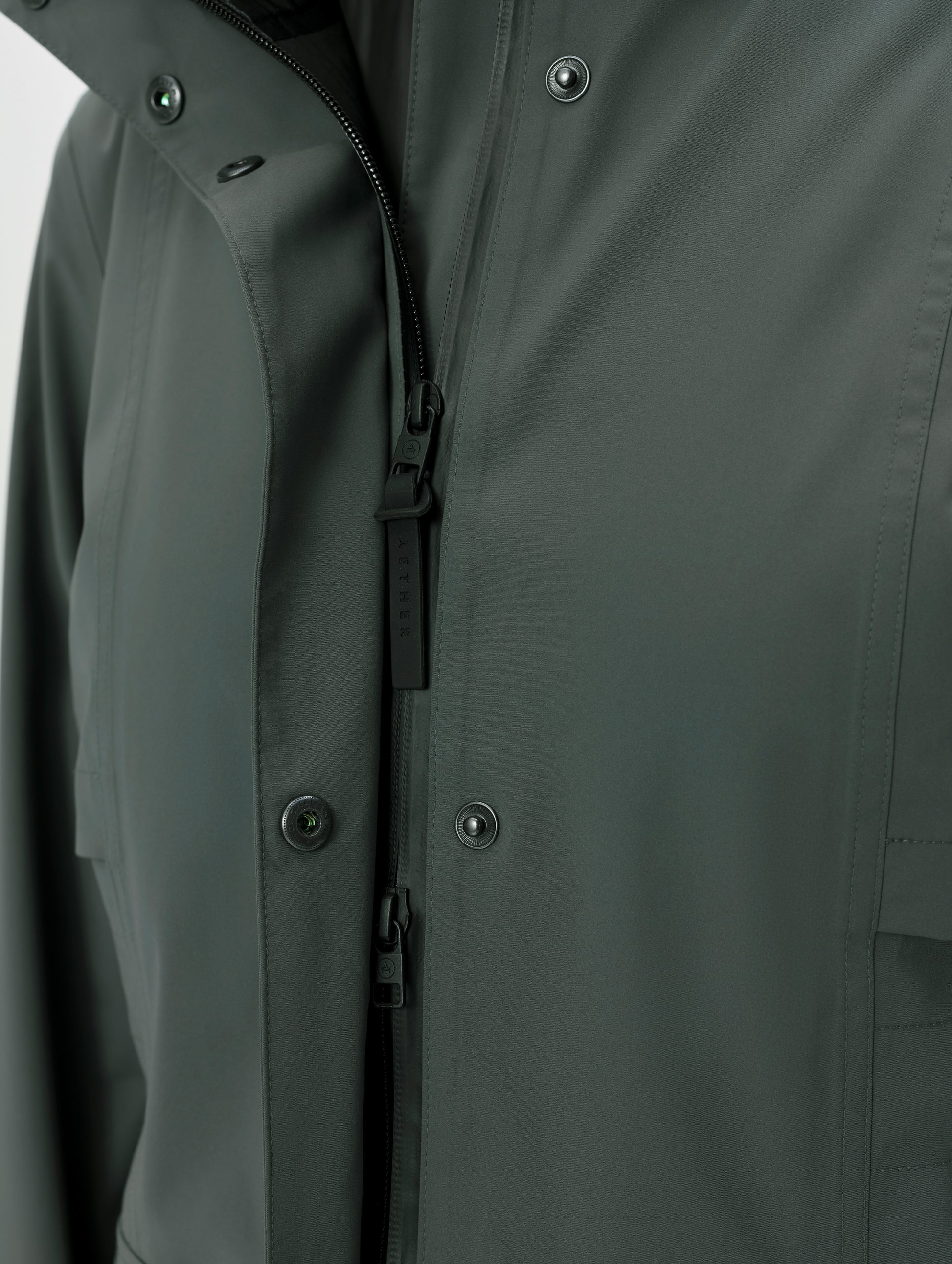 Closeup detailed view of the two-way main weatherproof center-front zipper on the women's Wallace Rain Parka in Saville Green from AETHER Apparel.