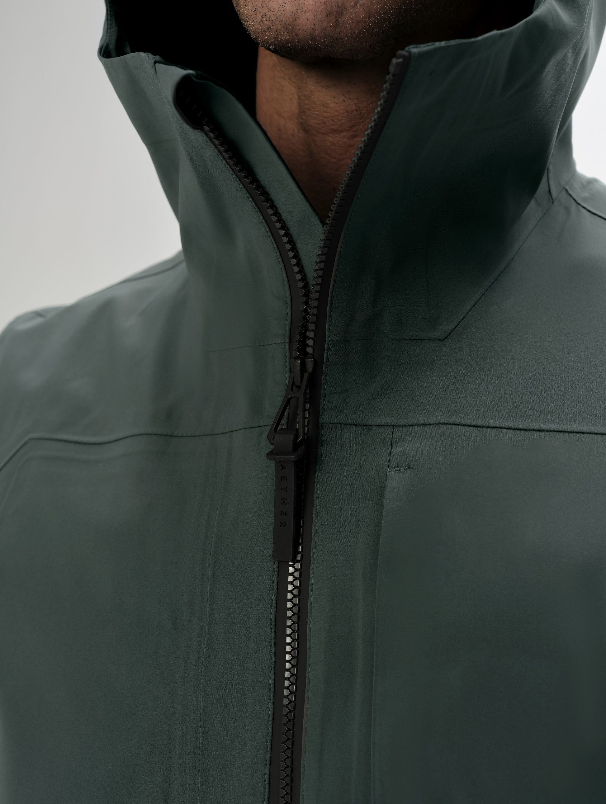 Closeup detailed view of the collar and center-front zipper on the men's Wallace Rain Parka in Saville Green from AETHER Apparel.