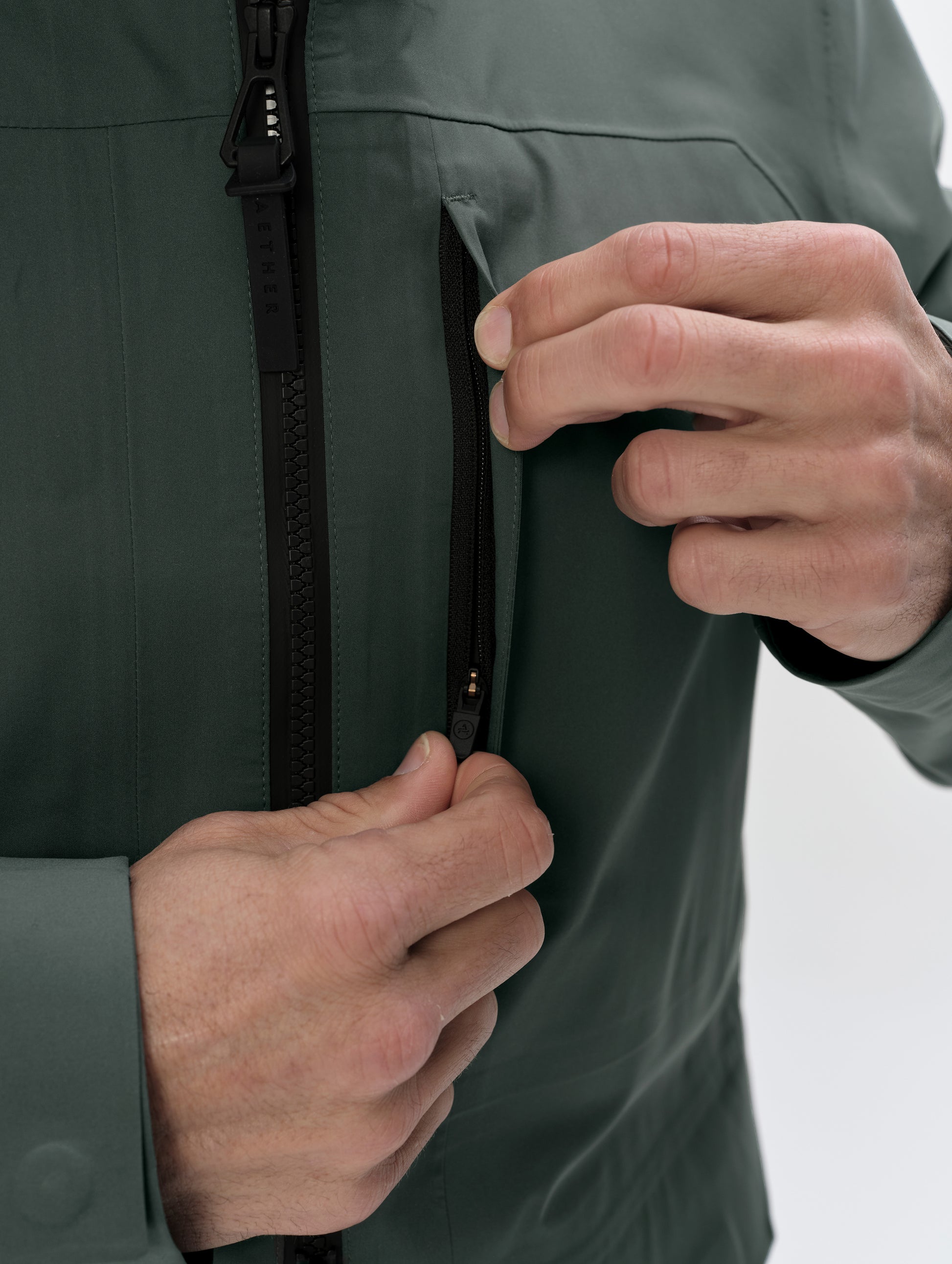 Closeup detailed view of the zippered chest pocket on the Wallace Rain Parka in Saville Green from AETHER Apparel. 