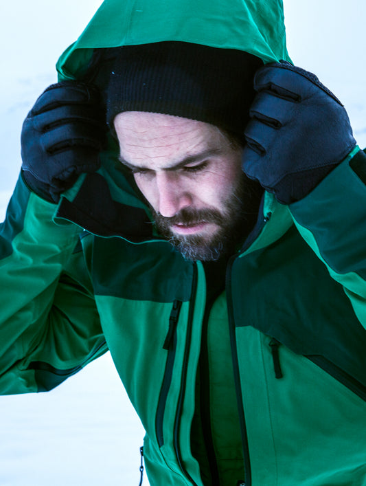 Man outdoors holding his hood wearing green Fusion Shell from AETHER Apparel.