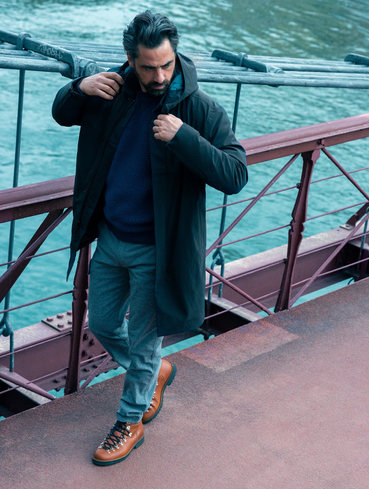 Outdoor lifestyle image of man walking on bridge wearing Isaac Jacket in Onyx Black from AETHER Apparel.