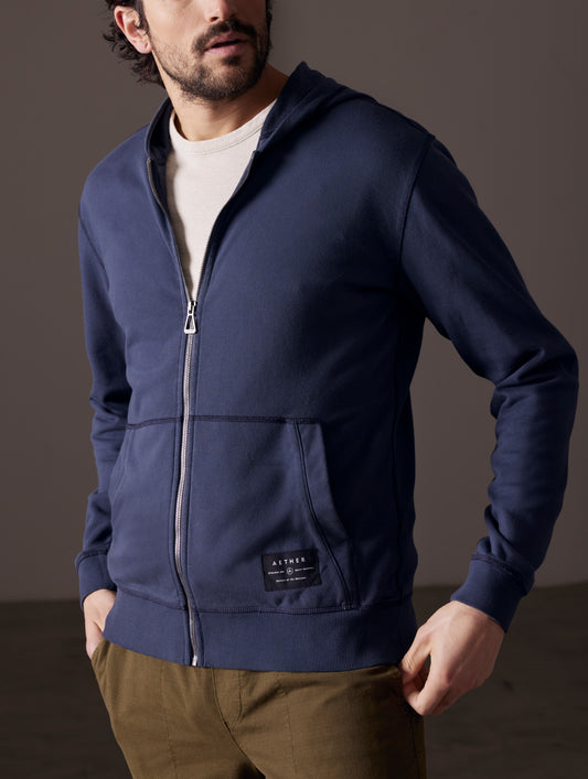 Front 3/4 body view of man wearing partially-unzipped Solstice Lightweight Full-Zip Hoodie in Total Eclipse dark blue from AETHER Apparel.