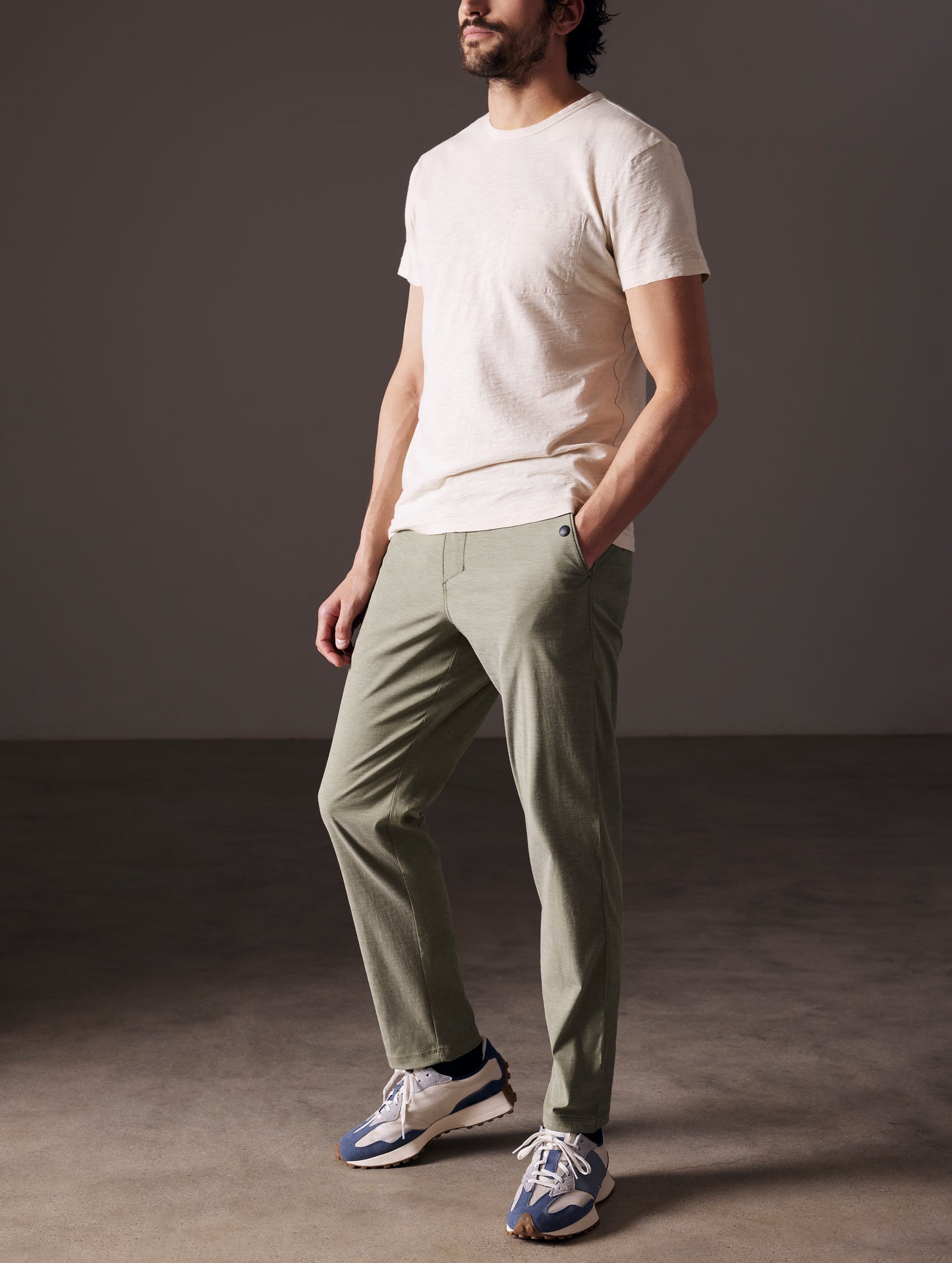 Front angled full-body view of man wearing Strand Tech Pant in Command Green from AETHER Apparel.