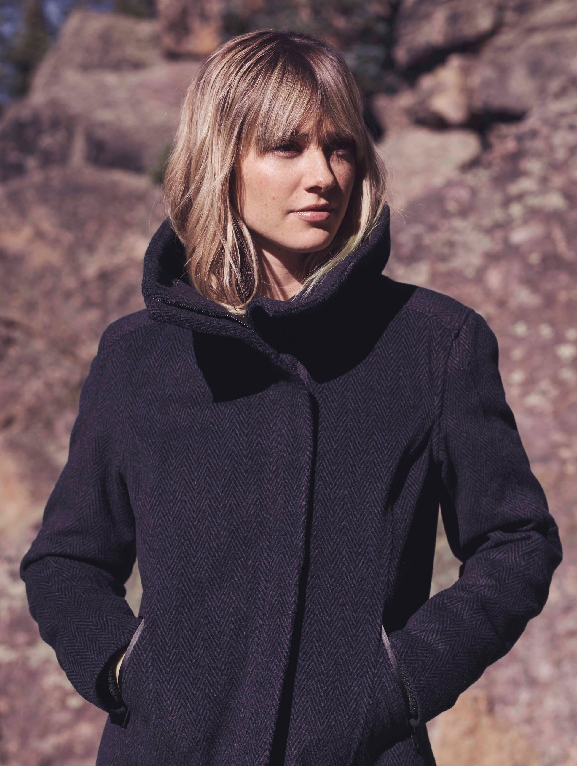 Upper body view of woman outdoors wearing blue Crosby Jacket from AETHER Apparel.