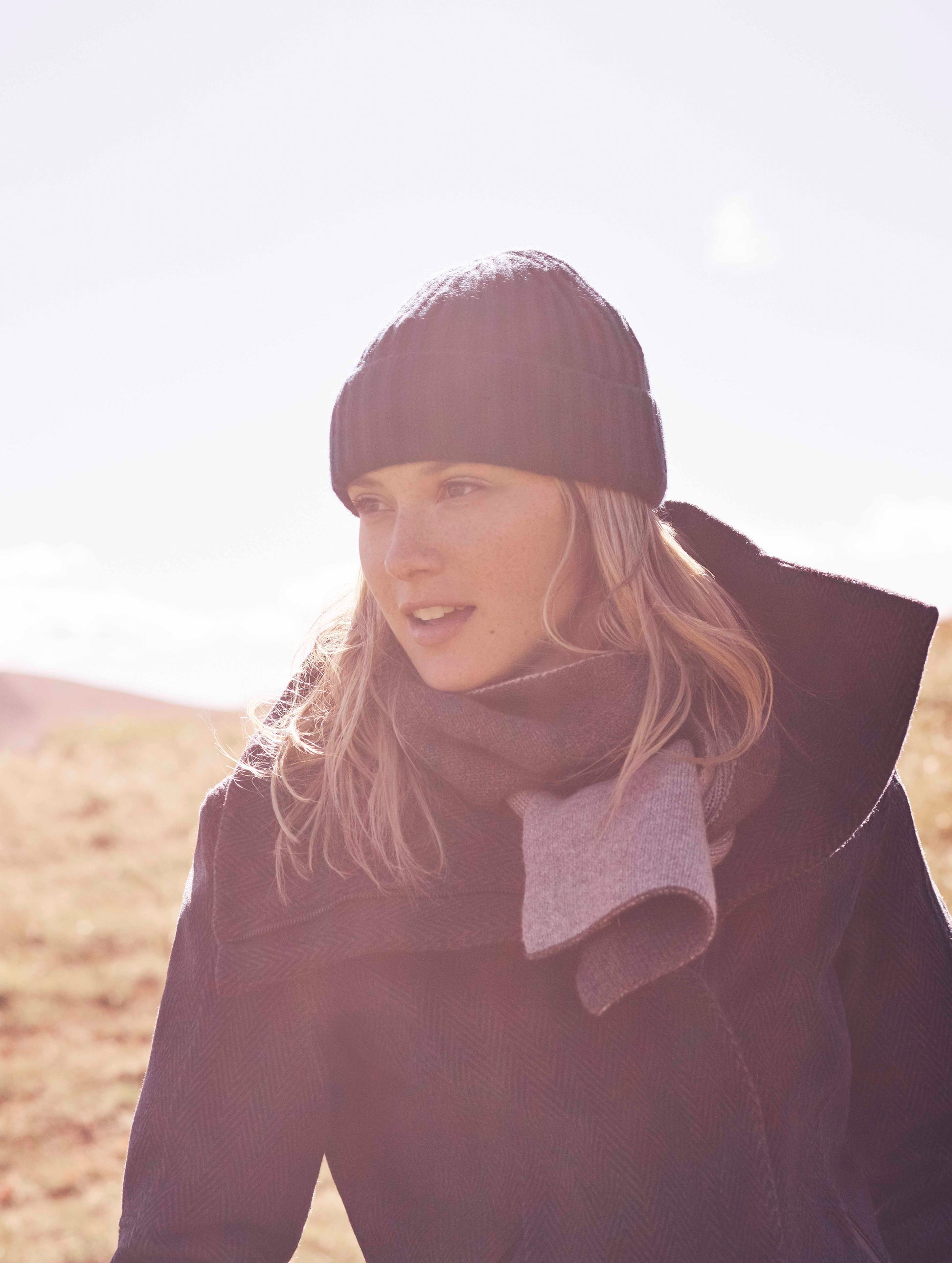 Close view of woman outdoors wearing blue Crosby Jacket from AETHER Apparel styled with hat and scarf.