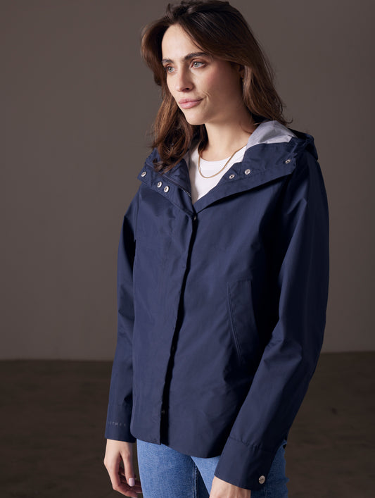 Front angled view of woman wearing Storm All-Weather Jacket in Total Eclipse dark blue from AETHER Apparel.