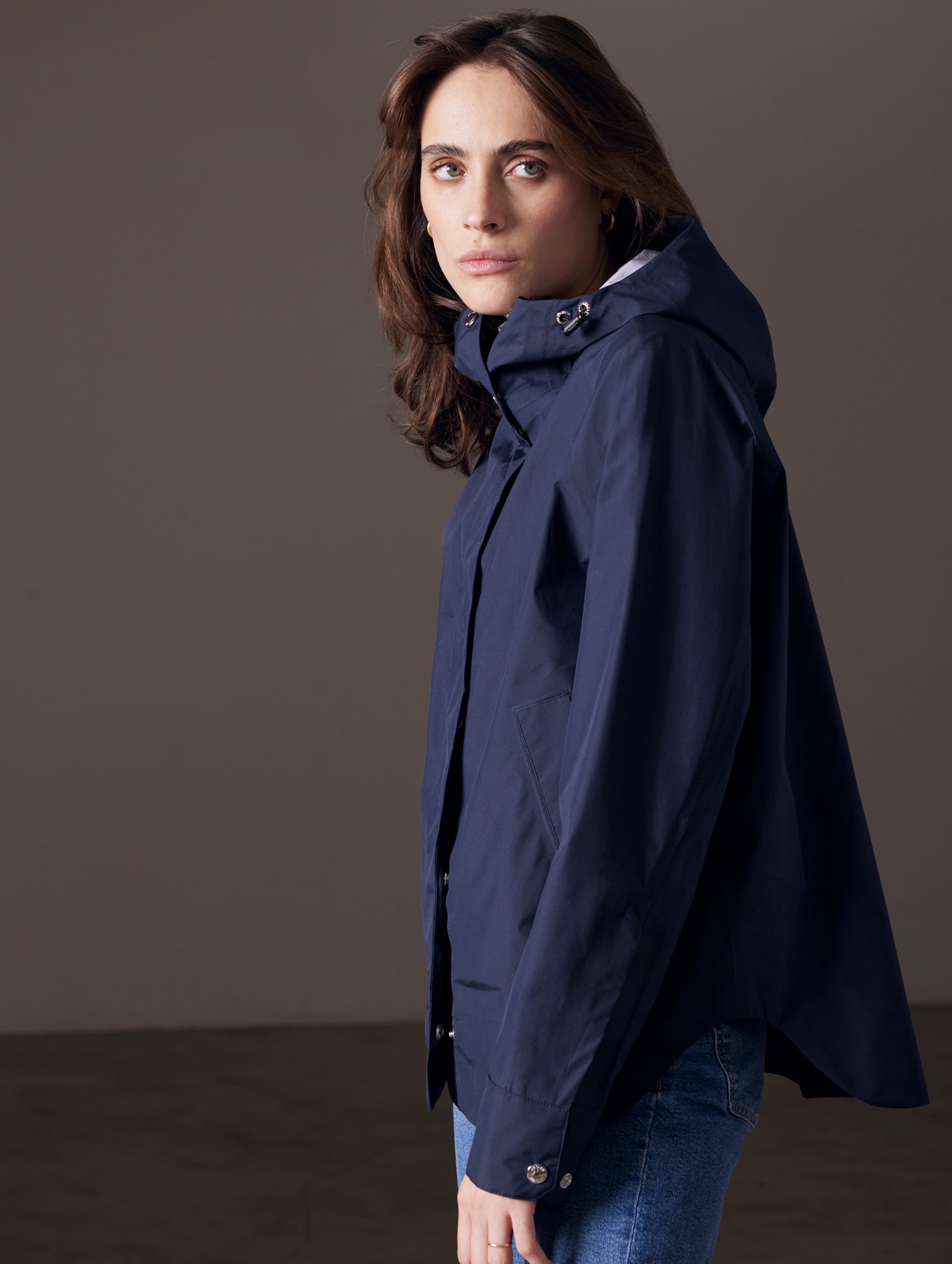 Side profile view of woman wearing Storm All-Weather Jacket in Total Eclipse dark blue from AETHER Apparel.