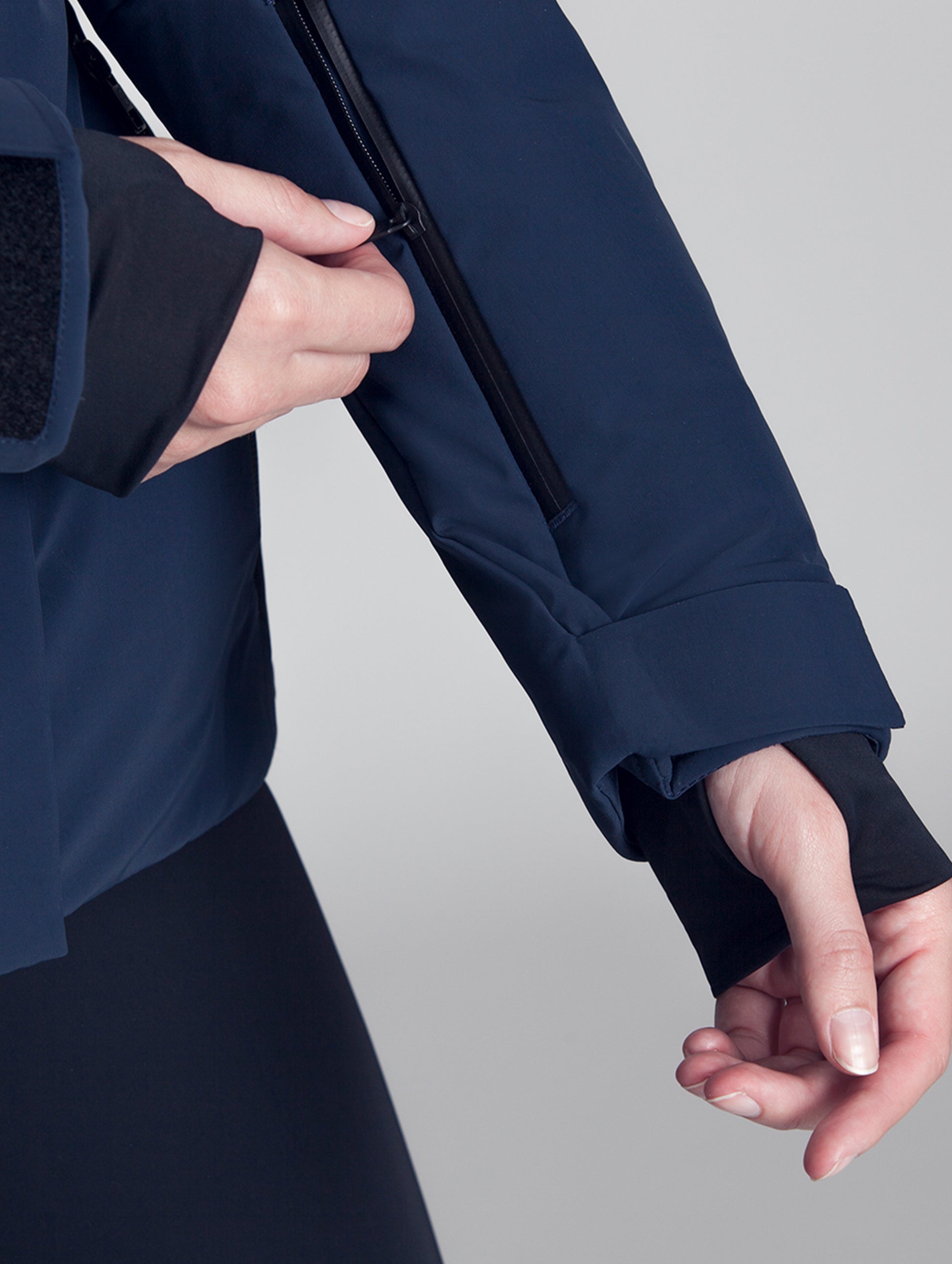 Woman wearing blue Vertical Jacket from AETHER Apparel, opening zippered pass pocket on her left sleeve.